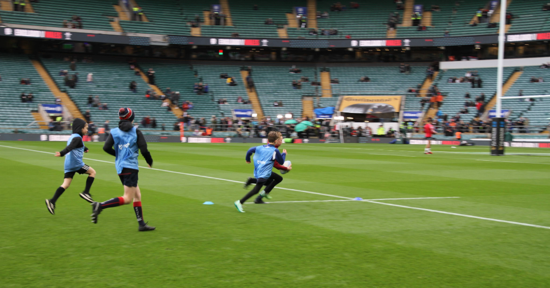 3 young rugby players training in a stadium setting, wearing blue bibs.